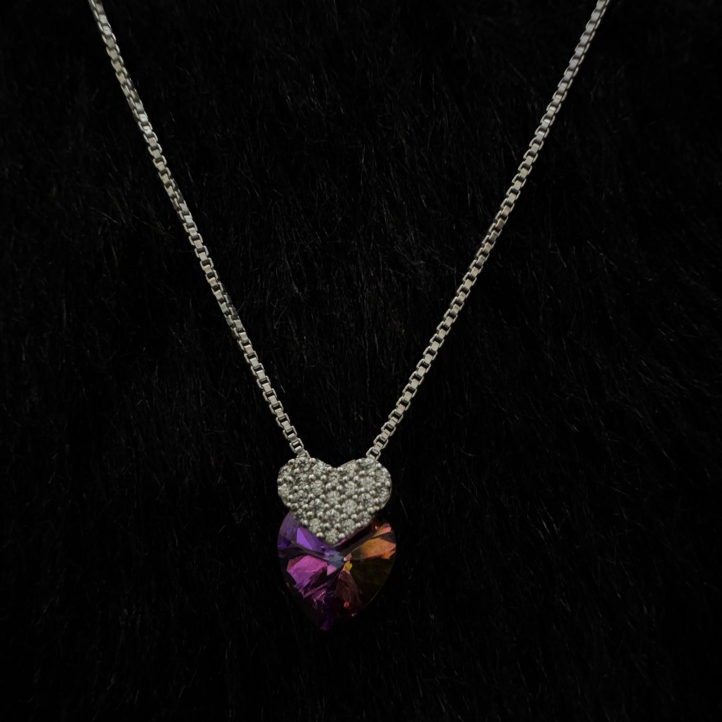 A stunning sterling silver necklace featuring a multicolored heart-shaped crystal pendant paired with a smaller, cubic zirconia-encrusted heart charm, elegantly displayed against a dark background.