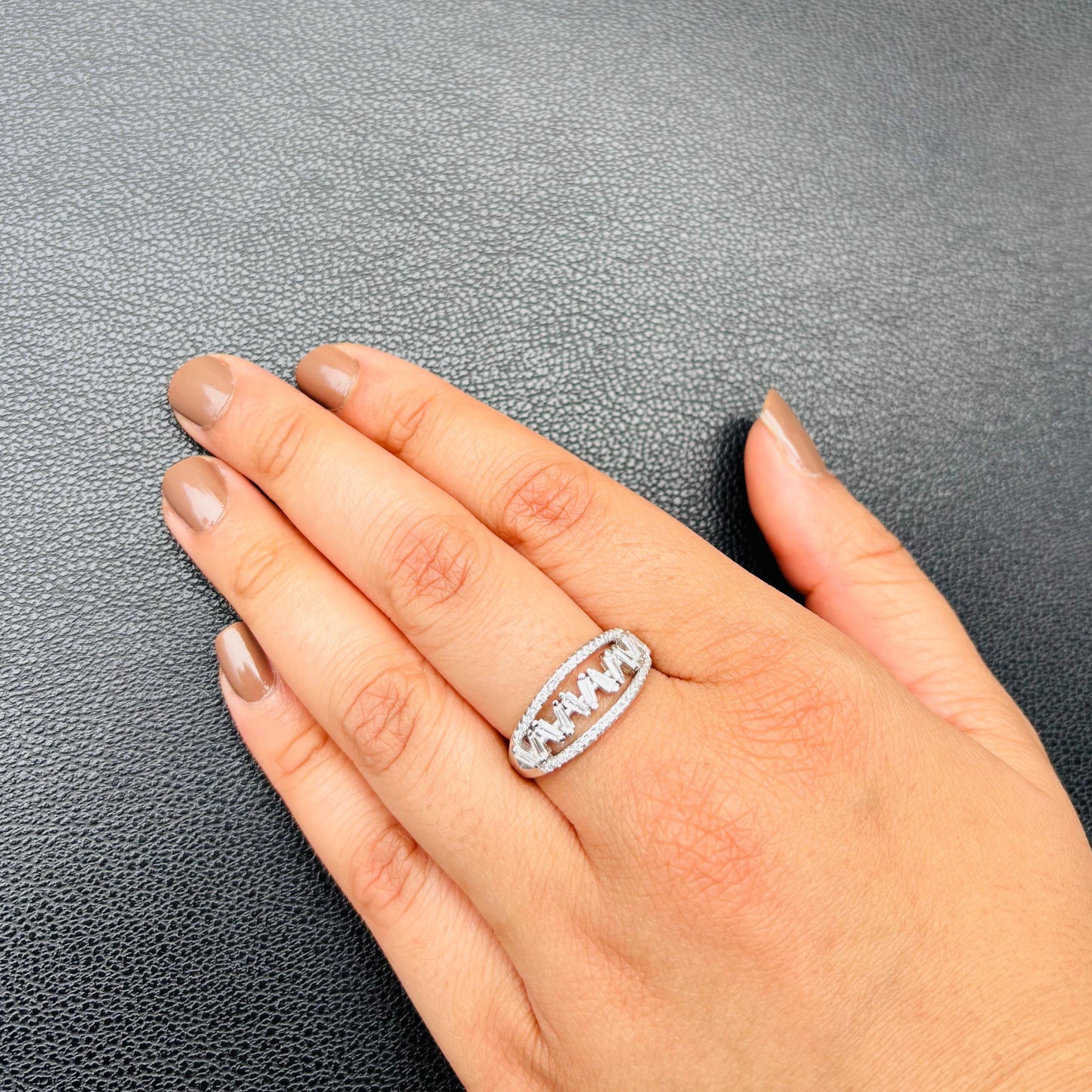 An exquisite sterling silver ring with an oval cutwork design encrusted with sparkling CZ stones, styled on a hand against a textured black background.