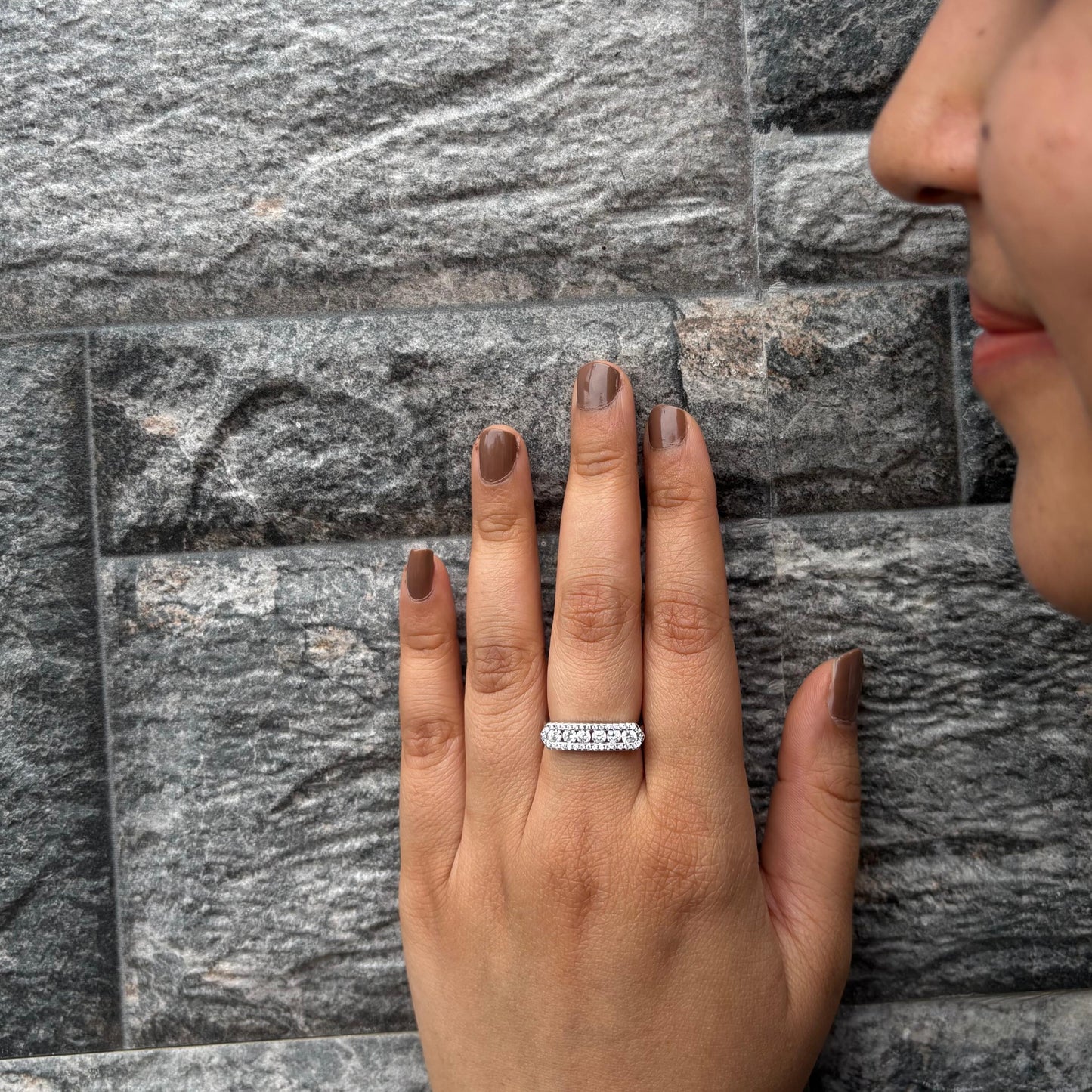 A sterling silver eternity band ring featuring sparkling CZ stones, elegantly worn on a hand with a gray textured stone wall in the background, showcasing refined simplicity.