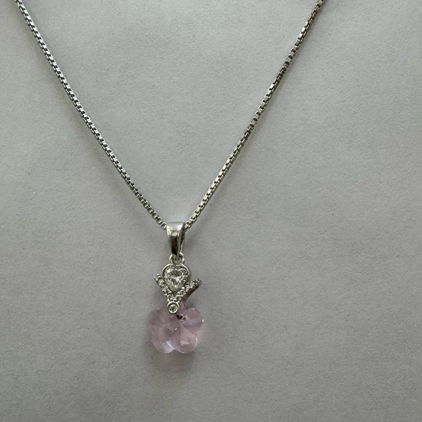 A sterling silver necklace with a pink heart-shaped crystal pendant, accented by a teardrop cubic zirconia and floral designs, displayed on a textured black and gold surface.
