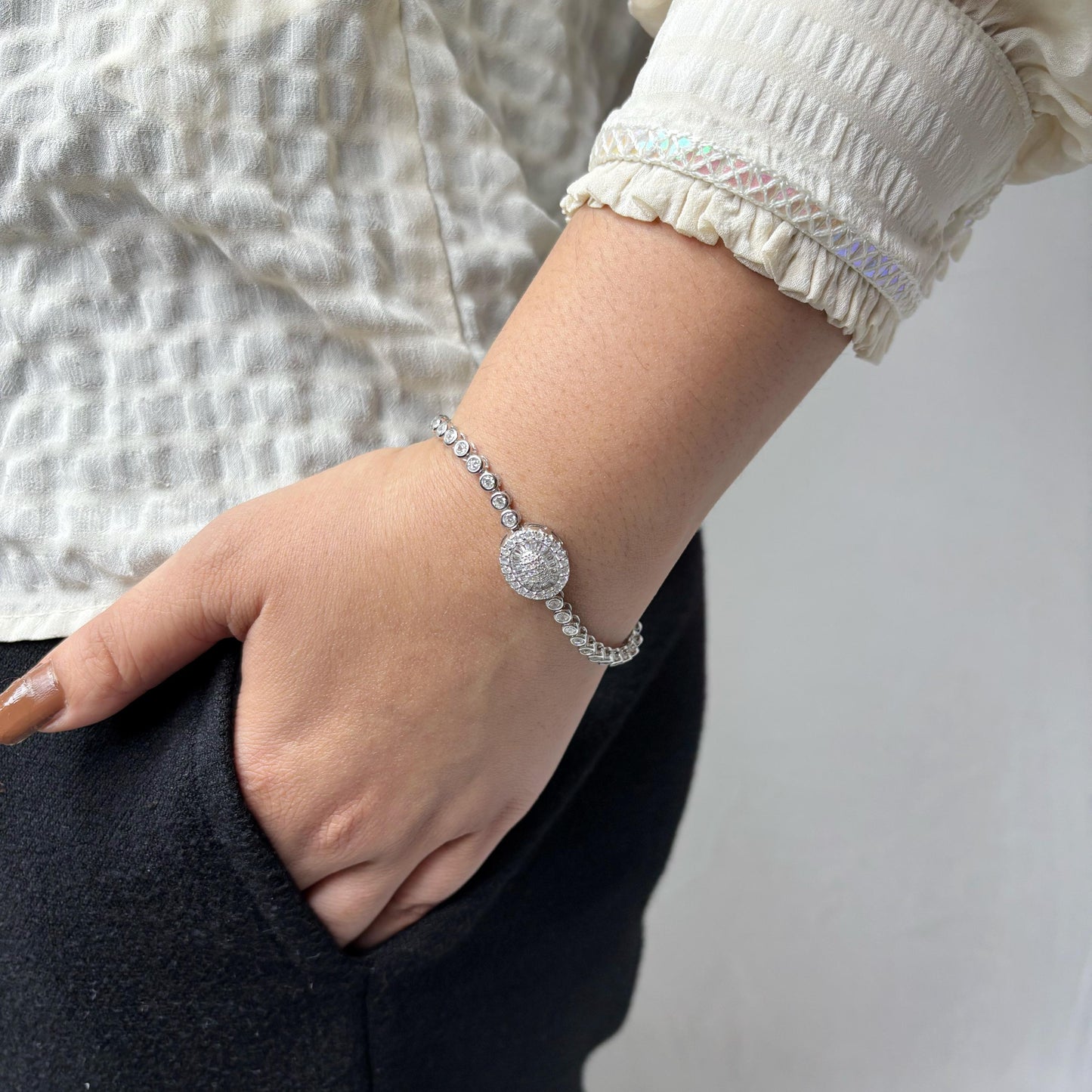 925 sterling silver bracelet with a round halo centerpiece of sparkling CZ stones, worn on a woman's wrist against a soft neutral background.