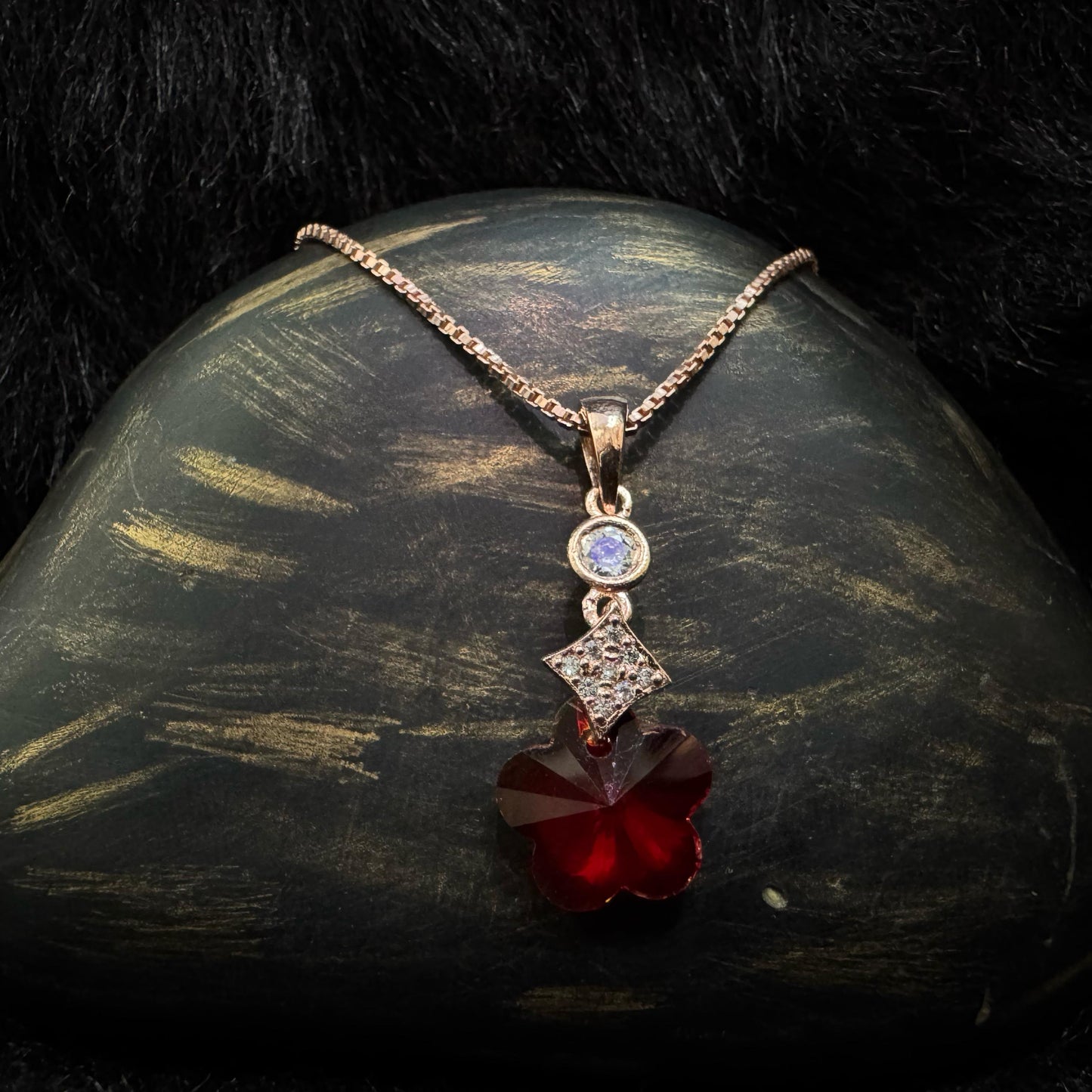 A rose-gold-toned sterling silver necklace featuring a vibrant red Swarovski crystal in a starburst shape, paired with cubic zirconia and moonstone accents, elegantly displayed against a textured dark backdrop.