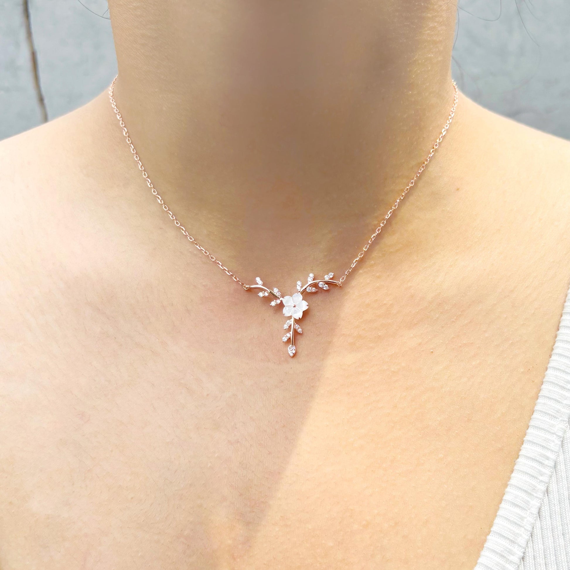 A delicate floral sterling silver necklace with rose-gold plating, featuring a blooming flower and branch design, worn on a woman to showcase its intricate elegance.