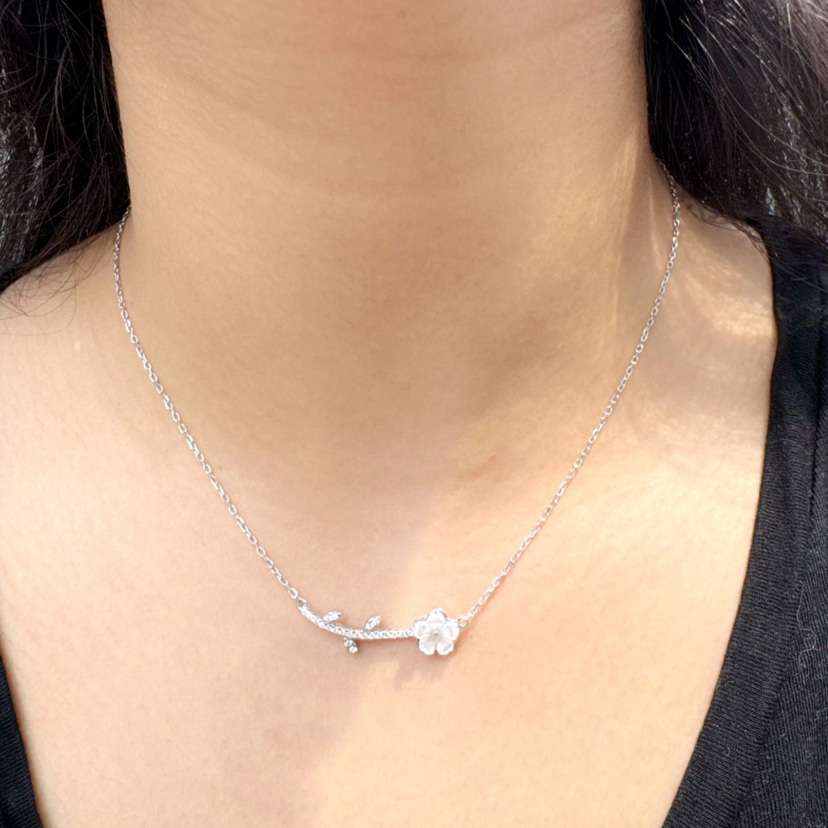 Minimalist sterling silver necklace with a floral branch design worn around the neck, featuring cubic zirconia accents for subtle sparkle