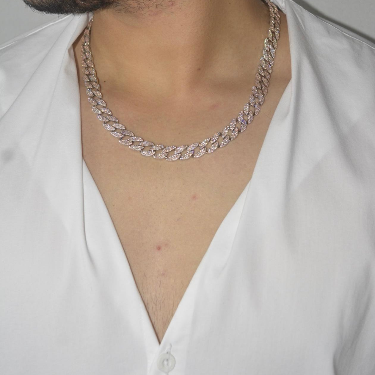 Rose gold tone Cuban link necklace encrusted with sparkling zircon stones on a model wearing a white V-neck top.