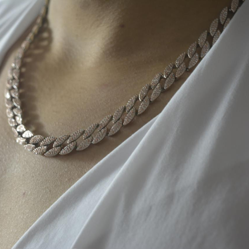 Rose gold tone Cuban link necklace encrusted with sparkling zircon stones on a model wearing a white V-neck top.