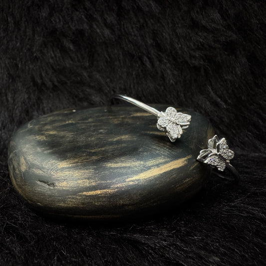 Elegant silver bangle bracelet with two butterfly-shaped ends adorned with sparkling cubic zirconia, displayed on a dark stone with a soft black background.