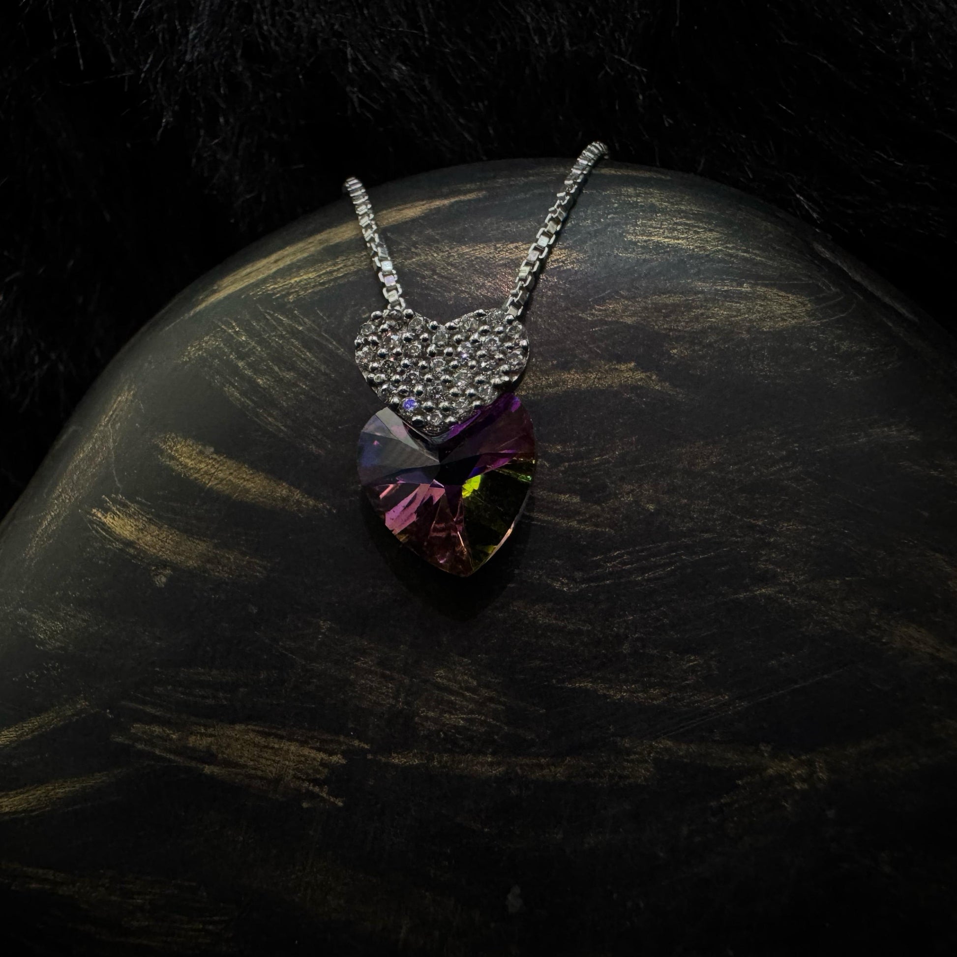 A stunning sterling silver necklace featuring a multicolored heart-shaped crystal pendant paired with a smaller, cubic zirconia-encrusted heart charm, elegantly displayed against a dark background.