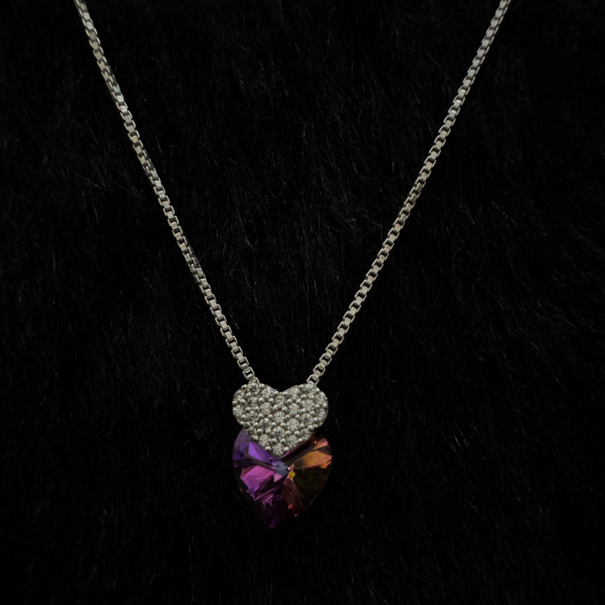 A stunning sterling silver necklace featuring a multicolored heart-shaped crystal pendant paired with a smaller, cubic zirconia-encrusted heart charm, elegantly displayed against a dark background.