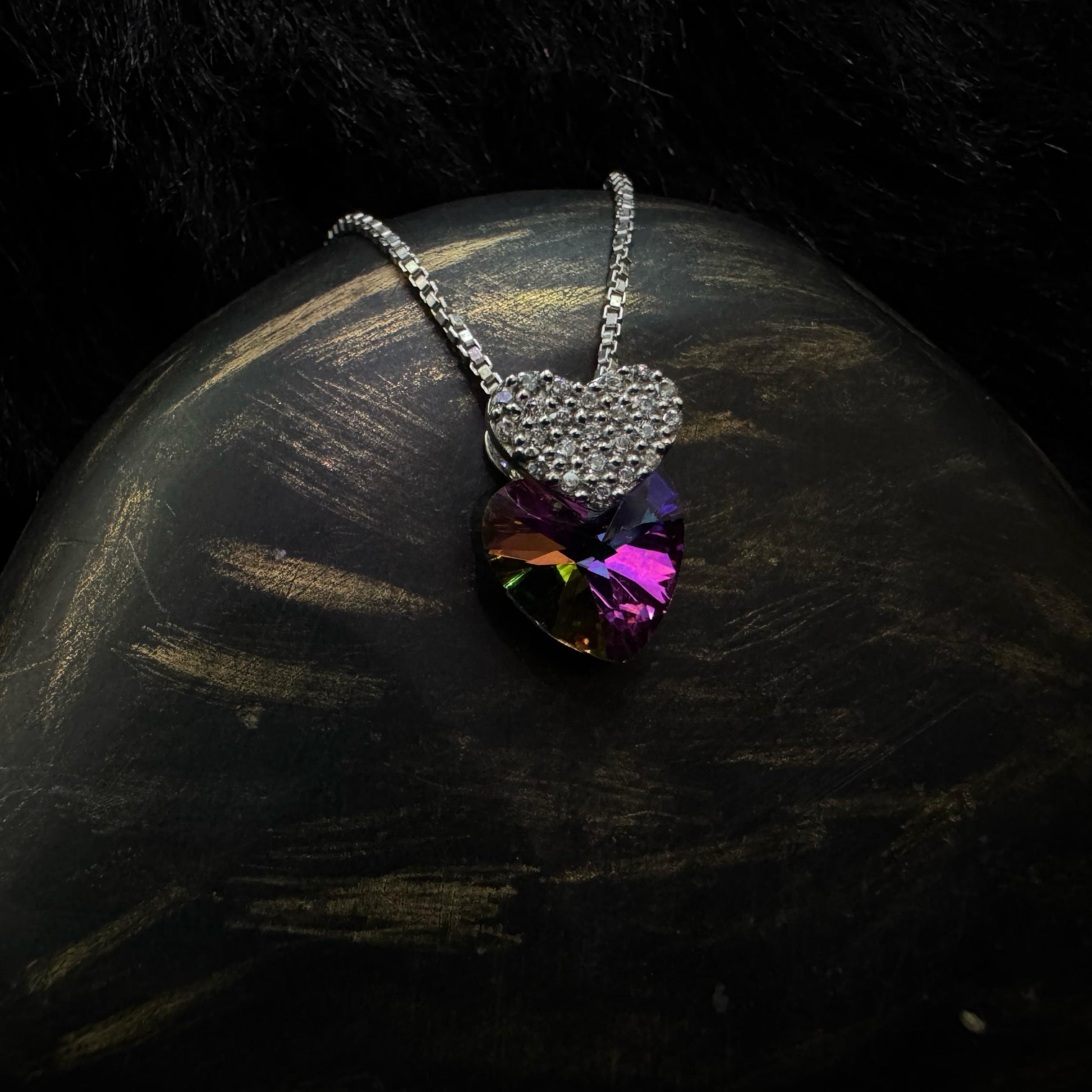 A stunning sterling silver necklace featuring a multicolored heart-shaped crystal pendant paired with a smaller, cubic zirconia-encrusted heart charm, elegantly displayed against a dark background.