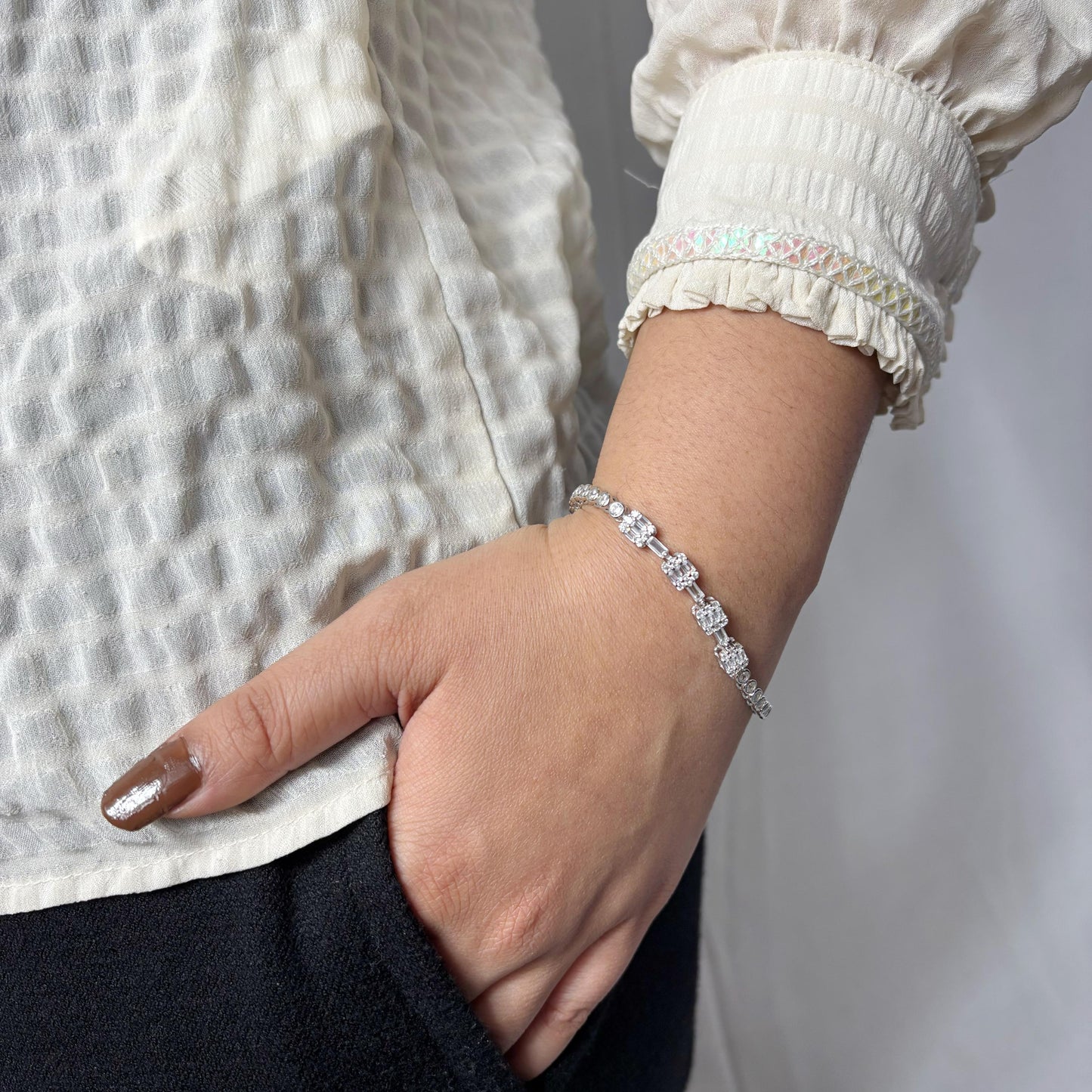 Elegant 925 sterling silver bracelet featuring alternating crystal-studded floral motifs worn on a woman's wrist, paired with a textured cream blouse.