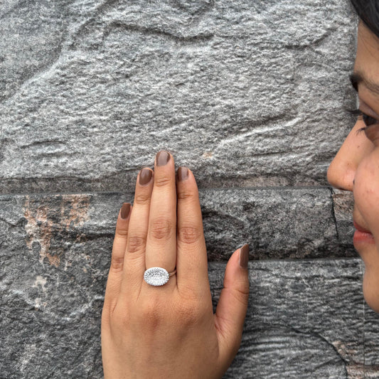 A sterling silver oval ring with a halo of sparkling CZ stones, elegantly worn on a hand.