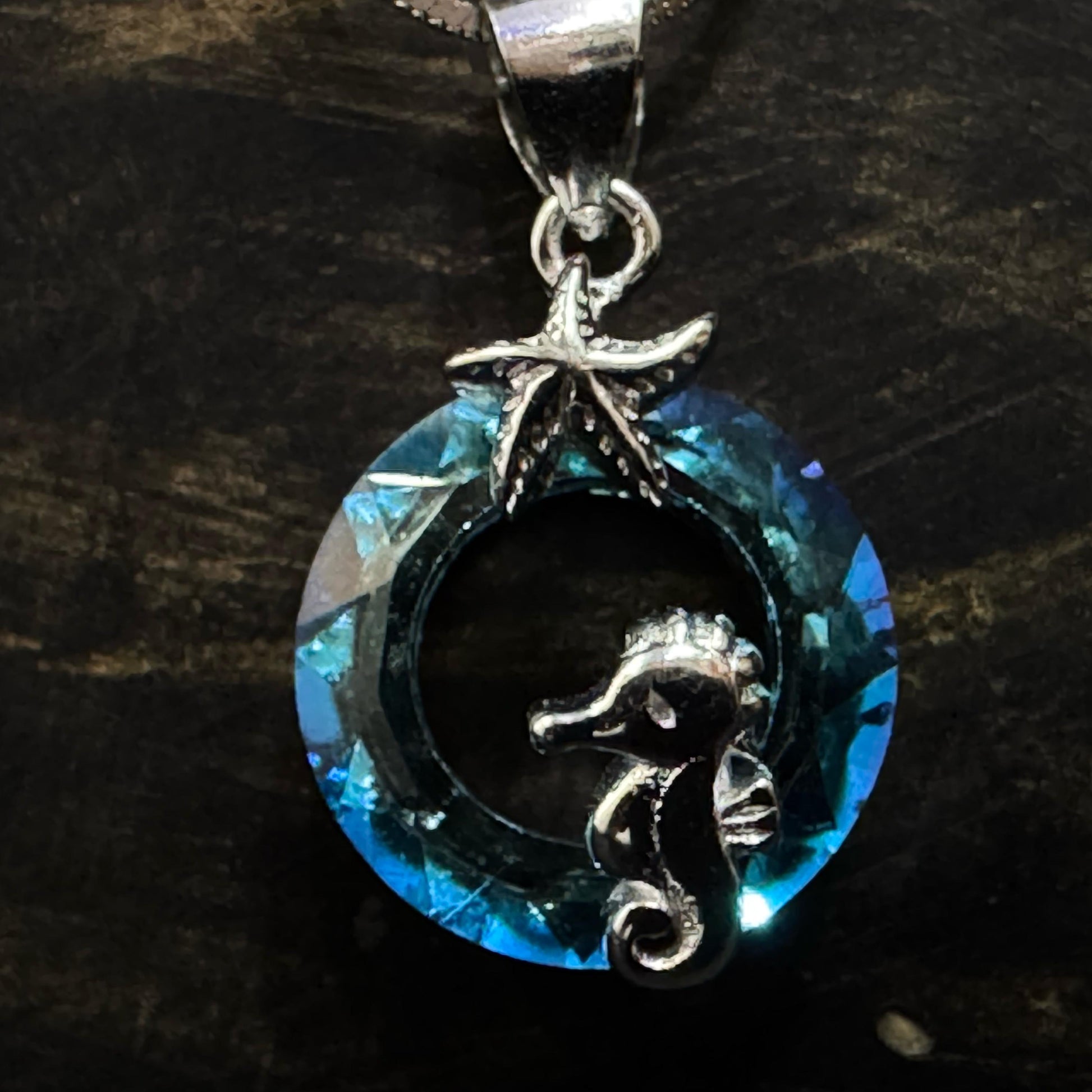 A silver necklace featuring a circular blue crystal pendant with a silver seahorse and starfish detail, displayed on a white background.