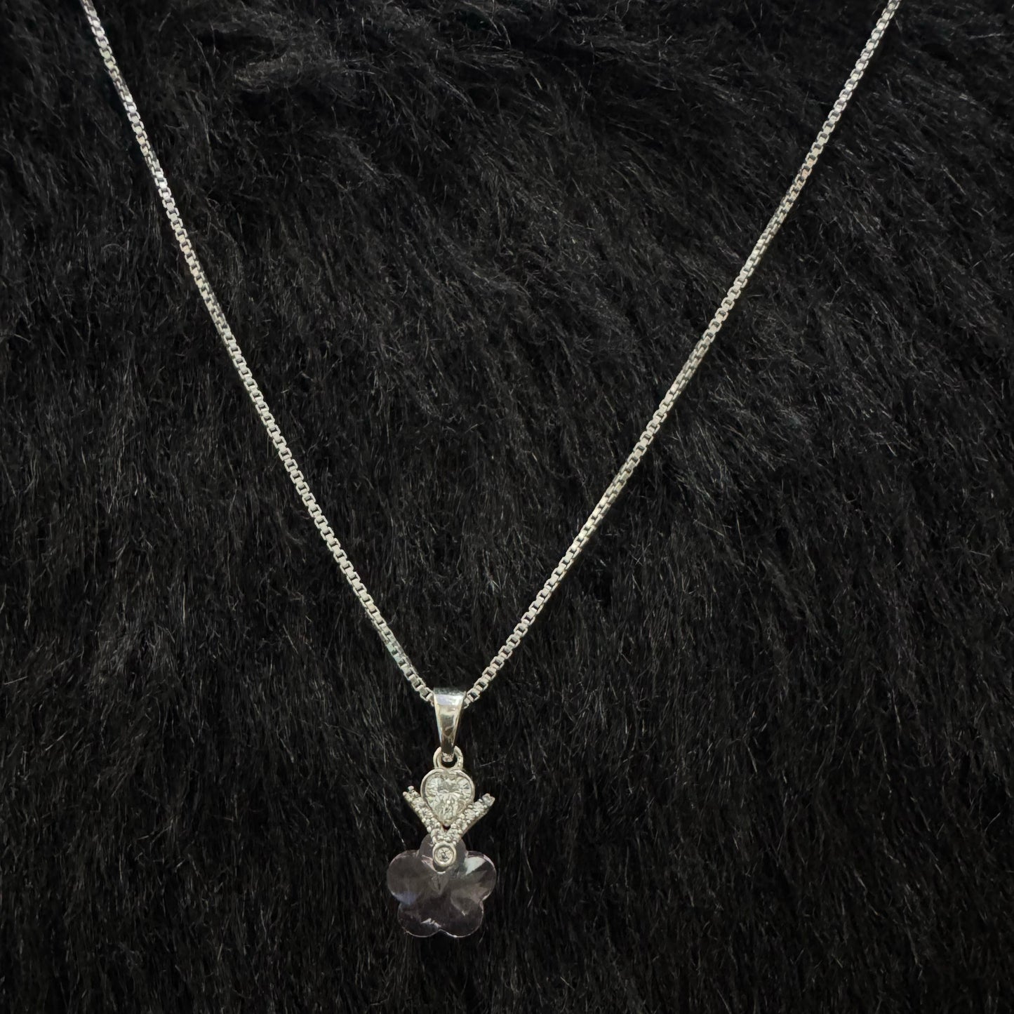 A sterling silver necklace with a pink heart-shaped crystal pendant, accented by a teardrop cubic zirconia and floral designs, displayed on a textured black and gold surface.