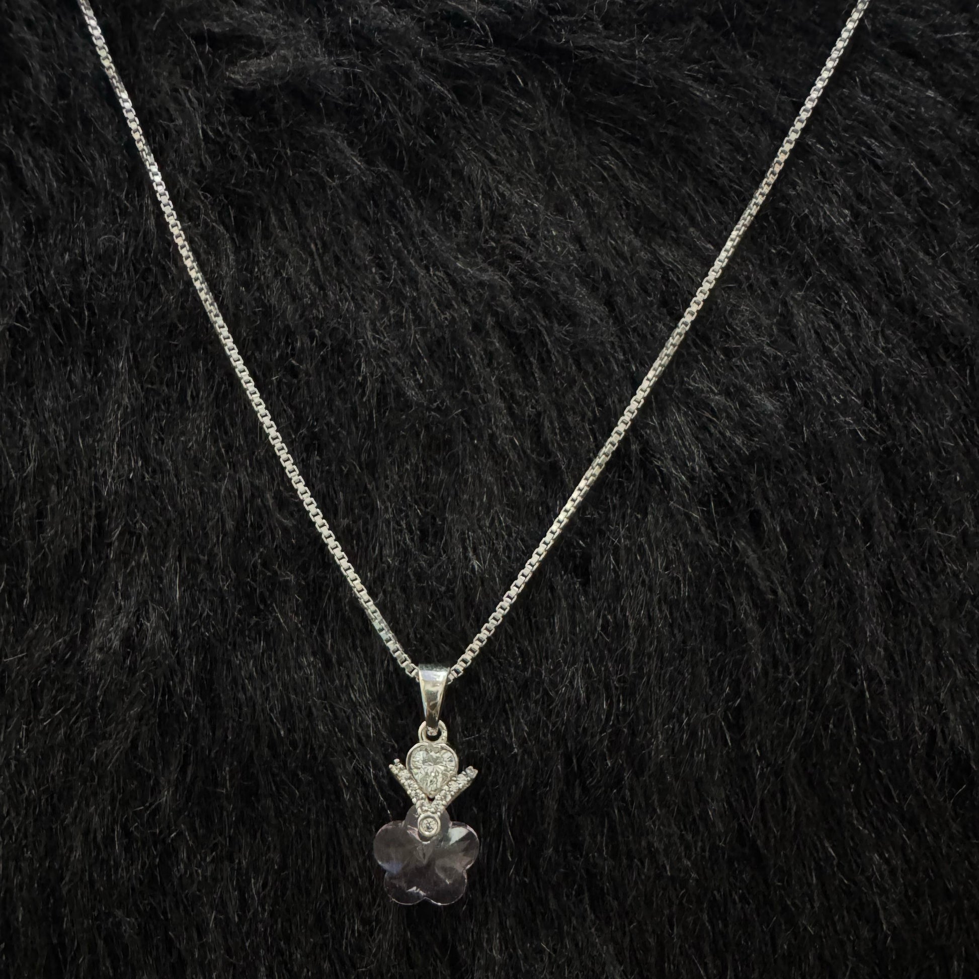 A sterling silver necklace with a pink heart-shaped crystal pendant, accented by a teardrop cubic zirconia and floral designs, displayed on a textured black and gold surface.