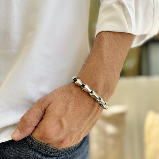 A chevron-pattern sterling silver bracelet adorning a man's wrist, styled with a white shirt and denim jeans, showcasing its sleek and modern design.