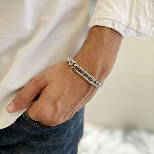 A sterling silver bracelet featuring a Greek key motif centerpiece with chain-link detailing, worn on a man's wrist styled with a white shirt and denim jeans, exuding timeless elegance.