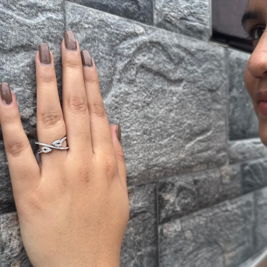 A twisted sterling silver ring with teardrop-shaped CZ stones, worn on a hand against a textured gray stone wall, reflecting a chic and modern design.
